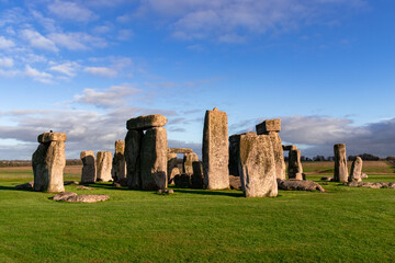 Naklejka premium A captivating view of Stonehenge, the iconic monument in England, illuminated by warm sunlight against a vibrant sky. The ancient stones stand tall on a lush green field