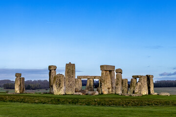 A stunning view of Stonehenge, the iconic prehistoric monument, set against a vibrant blue sky. The...