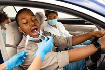Black Male Driver Getting Tested For Covid-19 Sitting In Automobile. Medical Worker Testing Family Of Three In Car, Wearing Protective Gloves. Healthcare And Transportation. Selective Focus