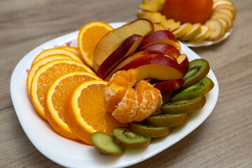 Sliced tropical fruits such as oranges, tangerines, bananas, kiwis, apples, persimmon lie on plates