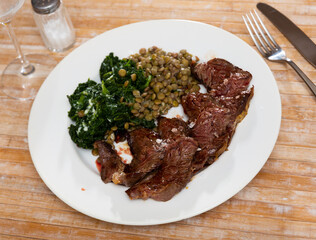 Appetizing hot beef in sauce served with spinach and lentils on platter..