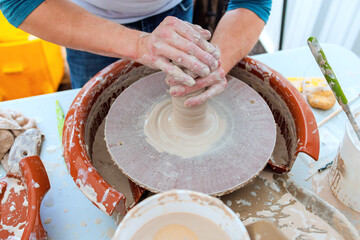 Potter hands skillfully shape wet clay on spinning wheel, showcasing craftsmanship in workshop art...