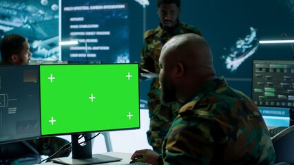 Soldier analyzing real time data next to green screen in high tech military office, processing...
