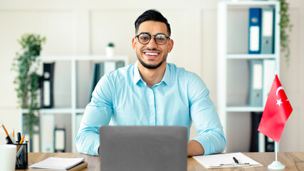 Portrait of millennial guy teacher with laptop teaching Turkish online from home, smiling at camera. Confident Arab guy tutor conducting educational web conference or webinar