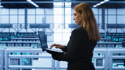 Technician doing yearly maintenance checkup using laptop to prolong data center hardware life span. IT specialist in server hub monitoring server infrastructure using notebook, camera A