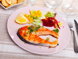 Delicious healthy dinner of baked salmon steak dressed with green sauce served with lemon slice and vegetables..