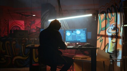 Hacker in hidden location with graffiti walls using PC to deploy malware on unsecured devices,...