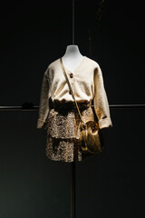 A stylish mannequin dressed in a cream cardigan, layered metallic gold skirt, and matching golden...