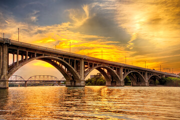 A bridge spans a river with a beautiful sunset in the background