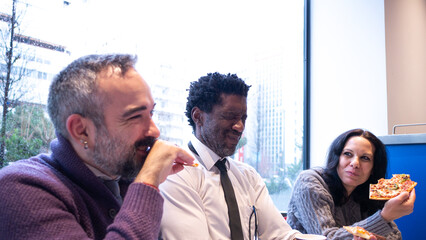 Three colleagues, including a bearded man, enjoying pizza and laughing together in a relaxed setting, capturing teamwork, joy, and a friendly office culture