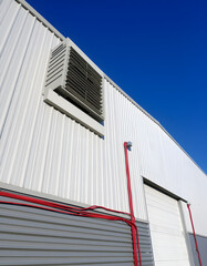 Large industrial warehouse with louver ventilation on aluminum corrugated wall with red cable lines wiring into building against blue sky background, perspective side view. isolated with white highl