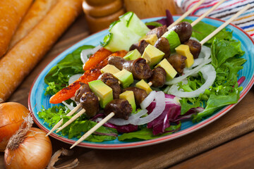 Skewers of chicken hearts with avocado served on platter with fresh vegetables and ingredients