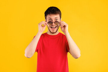 Wow. Portrait of man posing at studio, taking off sunglasses, looking at camera in amazement and with surprised facial expression isolated on blue background. It's Unbelievable. Summer Sale