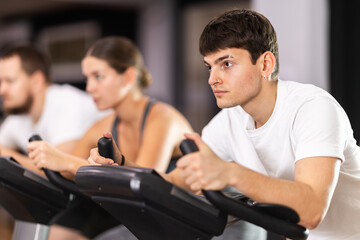 Young motivated guy training on an exercise bike in the gym