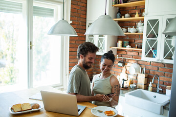 Happy couple looking at smartphone in cozy kitchen