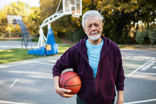 Portrait of a senior man holding basketball on outdoor court