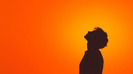 Silhouette of a person looking up at a vibrant orange sky.