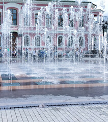 Jets of water in a fountain spurting from the ground, texture of the spray, urban fountain on the pavement
