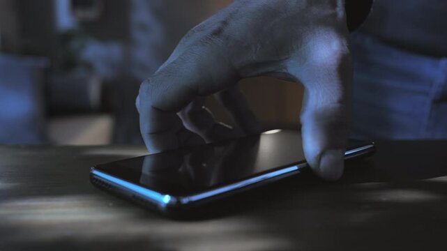male picking up mobile phone from table at night,person at home picks up smartphone from the desk in the dark room