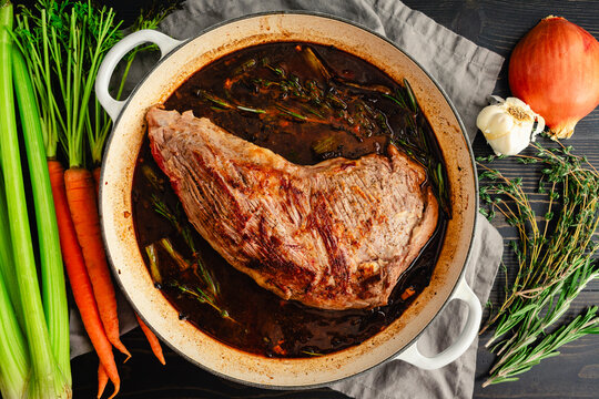 Braised Tri-Tip in Pan Surrounded by Herbs and Vegetables: Triptip roast beef and juices in enameled cast-iron braising pan surrounded by ingredients
