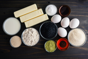 Matcha Black Sesame Babka Ingredients on a Wooden Table: Green tea powder, flour, eggs, honey, and more directly above rustic dark wood background
