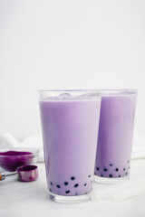 Two Glasses of Purple Sweet Potato Bubble Tea: Ube boba with ice cubes and clear silicone straws on a white background