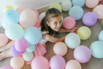 A surprised little girl with colorful balloons in pastel colors on a white background. Celebration, birthday, party, childhood concept. Top view