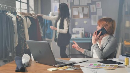 handcrafted artisan clothes entrepreneur working at the workshop,handmade clothing female designer at the desk phone calling client works in the studio with her business  partner