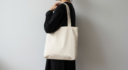 Canvas tote bag, minimalist design, cream color, black outfit, shoulder strap, white wall background, lifestyle photography, soft lighting