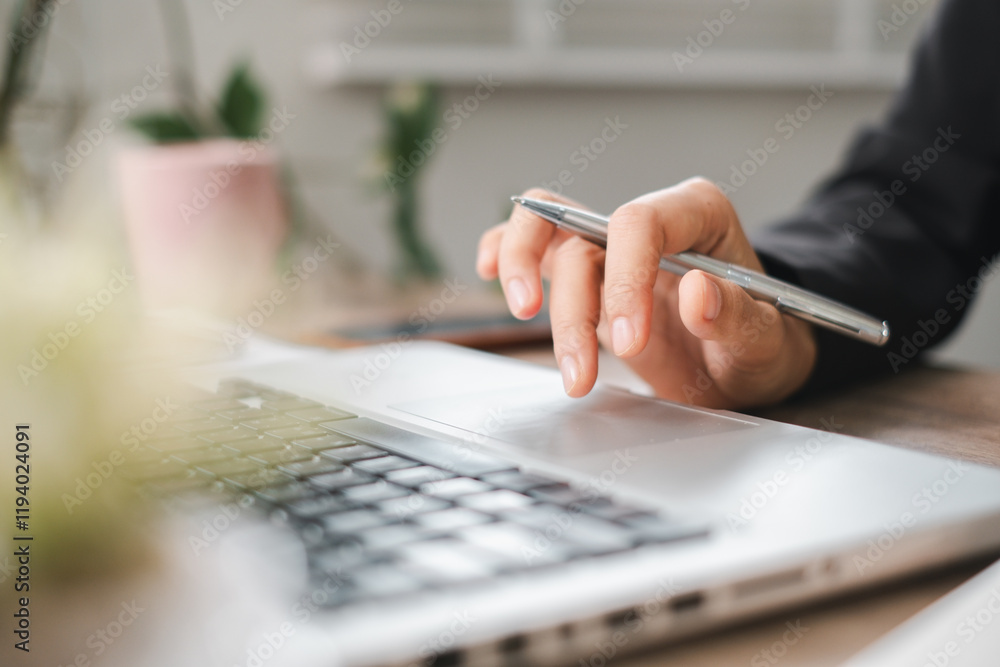 Poster close-up of hand using pen on laptop touchpad in modern office setting with greenery in background