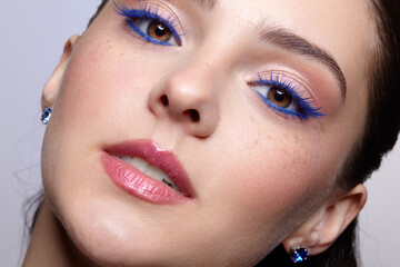 Close-up shot of female face with blue eyes arrows and lashes beauty makeup. Woman wears earrings with rhinestones in ears.