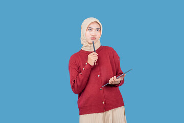 A woman wearing a red sweater and a tan head scarf is holding a pen tablet and looking up. She is...