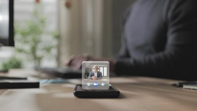 Person at the desk using computer receiving business video call on smart phone screen,co-workers having remote work online meeting briefing via virtual display app - Powered by Adobe