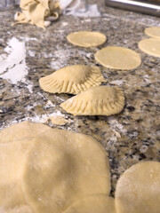 close-up of pierogies being stuffed and pressed and about to be fried, pierogies on a granite counter top with flour and fresh dough
