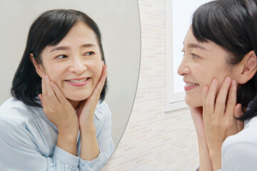 鏡を見て顔のスキンケアをする50代の女性