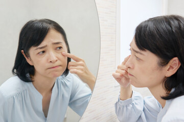 鏡で目元のクマを見て悩む50代女性