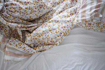 A disheveled bed adorned with vibrant, colorful floral bedding and a striking green headboard