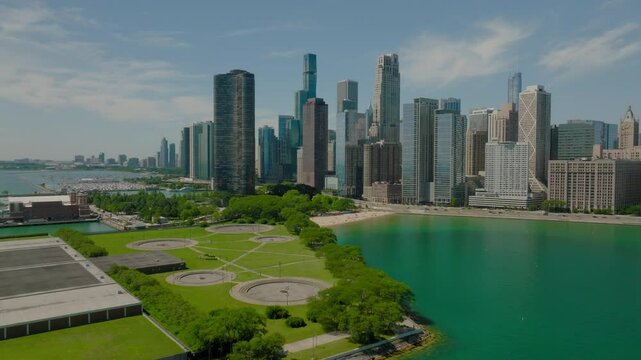 Aerial Shot Of Modern Office Buildings In Downtown District, Drone Flying Forward Over Milton Lee Olive Park On Sunny Day - Chicago, Illinois