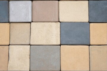 "Top-down close-up view of grid-like patterned wall with colorful and textured square tiles in varying shades from beige to grey."