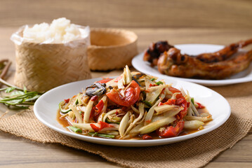 Spicy papaya salad (Som Tum) eating with sticky rice and grilled chicken wing on wooden table, Local Thai food