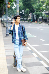 Fototapeta premium Young Asian Male Wearing Casual Style Standing on Sidewalk While Using Smartphone