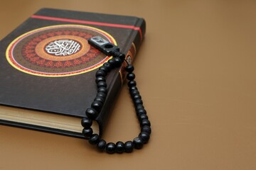 Al Quran with cover decorated with calligraphy that says (Al Quran) and prayer beads
