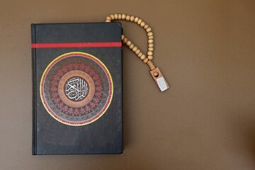 Al Quran with cover decorated with calligraphy that says (Al Quran)and brown prayer beads