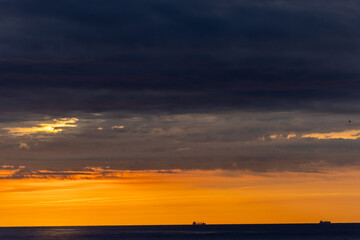 Stunning sunset over ocean, dramatic clouds, silhouetted ships on horizon, creating serene, majestic scene