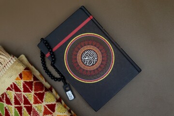 Prayer beads on top of the QuranAl Quran with cover decorated with calligraphy that says (Al Quran)