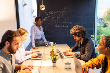Diverse team collaborating with laptops in a modern office, brainstorming growth and success strategies.
