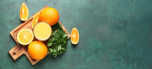 Wooden board with glass of tasty juice, oranges and mint leaves on green grunge background