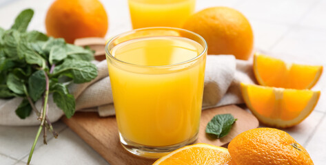 Glasses of tasty juice with oranges and mint leaves on white tile background
