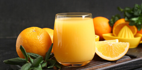 Wooden board with glass of tasty juice, oranges and leaves on black grunge background