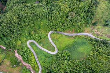Top view of countryside road passing through the green forrest and mountain